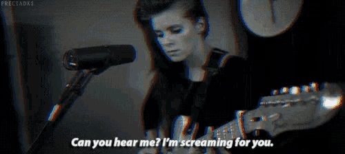 a woman is singing into a microphone in a dark room while screaming .