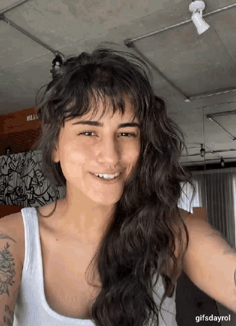 a woman wearing a white tank top is smiling for the camera with gifsdayrol in the corner