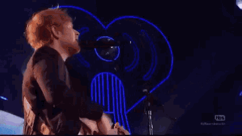 a man is singing into a microphone while playing a guitar in front of a heart shaped sign .