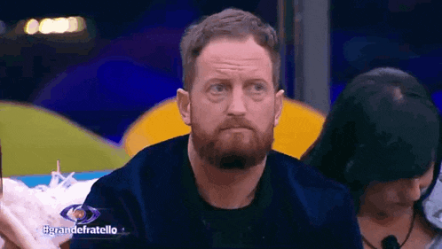 a man with a beard is sitting at a table with a sign that says grandefratello
