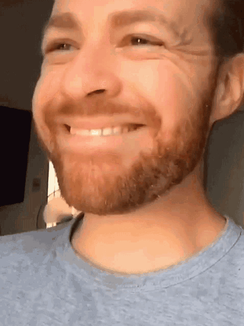 a man with a beard wearing a blue shirt smiles for the camera