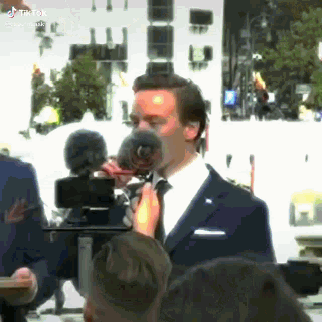 a man in a suit and tie is speaking into a microphone in front of a camera ..