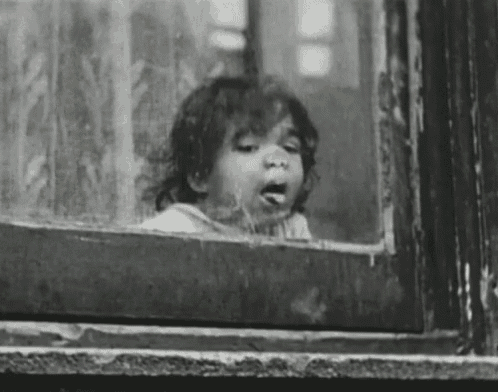 a black and white photo of a young girl looking out of a window .