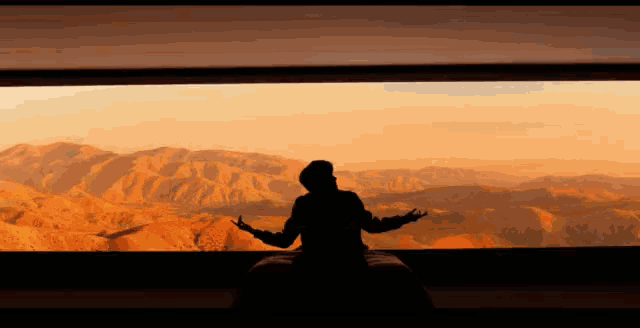 a silhouette of a man standing in front of a mountain range