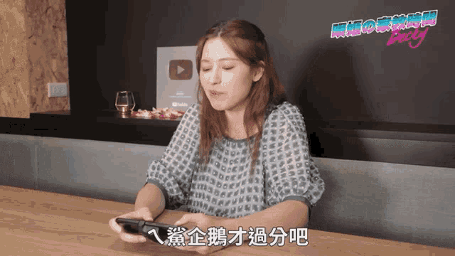 a woman is sitting at a table looking at her phone with chinese writing on the bottom