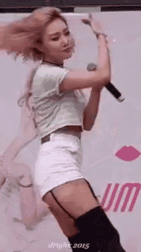 a woman in a crop top and white shorts is holding a microphone and dancing .