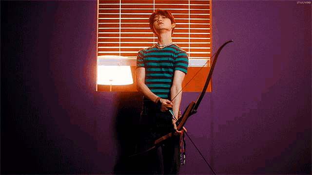 a man is holding a bow and arrow in front of a window with blinds