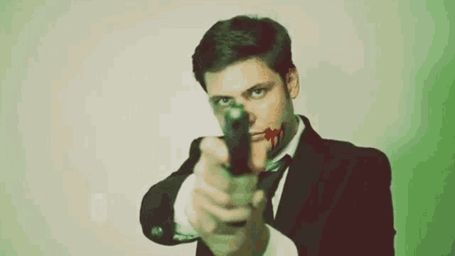 a young man in a suit and tie is pointing a gun at the camera .