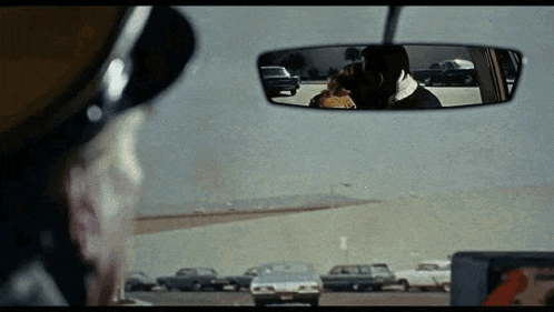 a man is looking at another man in the rear view mirror of his car .