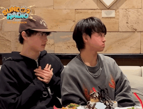 two boys are sitting at a table with a sign that says sundae radio