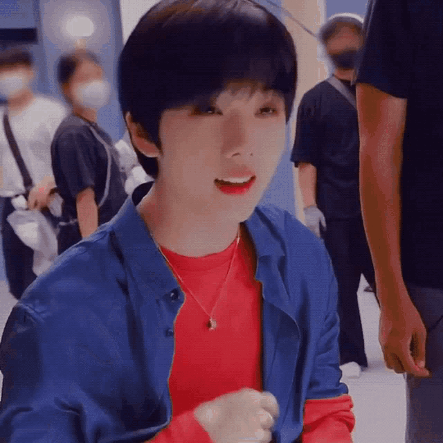 a young boy wearing a blue jacket and a red shirt is smiling while standing in a crowd .