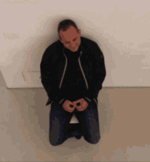 a man in a black jacket is kneeling down with his hands folded