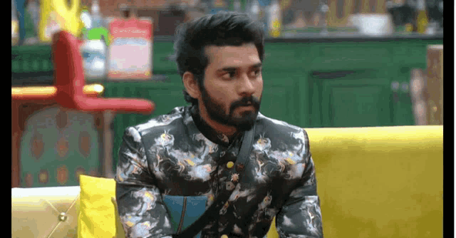 a man in a floral shirt is sitting on a yellow couch .