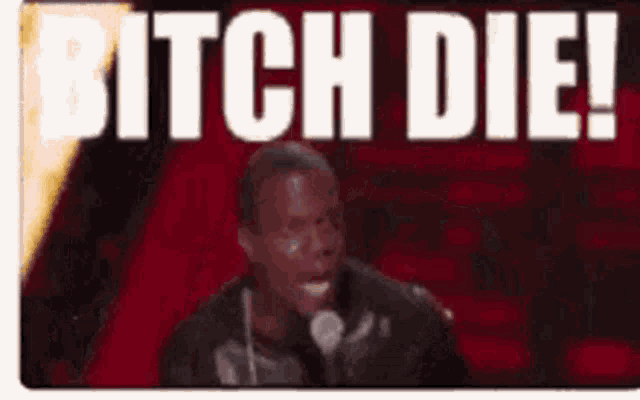 a man holding a microphone in front of a sign that says bitch die !