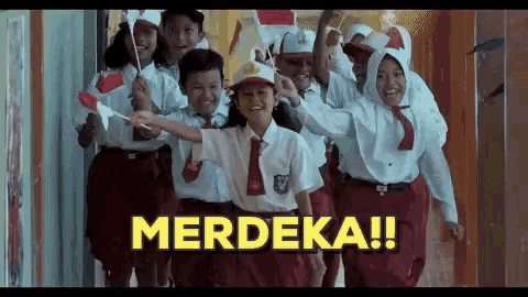 a group of children in school uniforms are walking down a hallway holding flags and a sign that says merdeka .