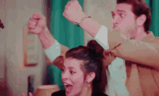 a man and a woman are sitting at a table with their hands in the air .