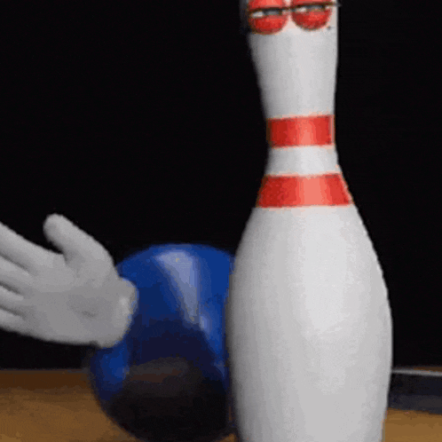 a bowling pin with a face painted on it is standing next to a blue bowling ball .