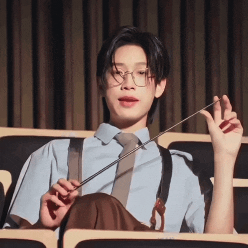 a young man wearing glasses and suspenders holds a baton