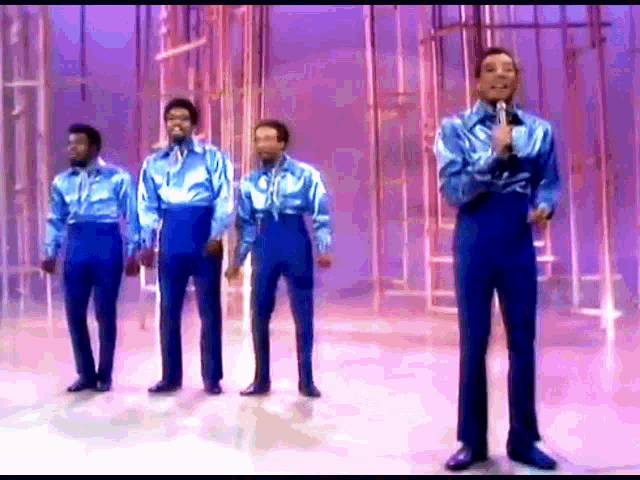a group of men in blue shirts and pants are singing on a stage