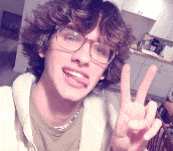 a young man with curly hair and glasses is giving the peace sign