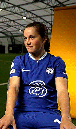 a woman is sitting in a chair on a soccer field wearing a blue shirt and shorts .