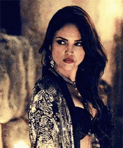 a woman wearing a black bra and a silver jacket looks at the camera