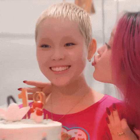 a woman with pink hair kisses another woman 's cheek