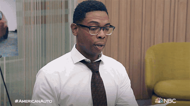 a man wearing glasses and a tie is sitting in front of a yellow chair ..