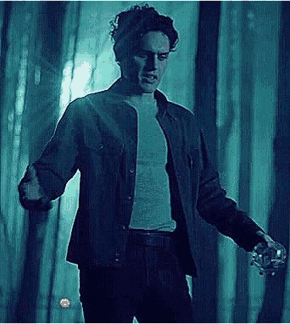 a man in a denim jacket and a white shirt is standing in a dark room .