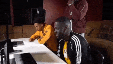 a group of men are sitting at a table looking at a laptop .