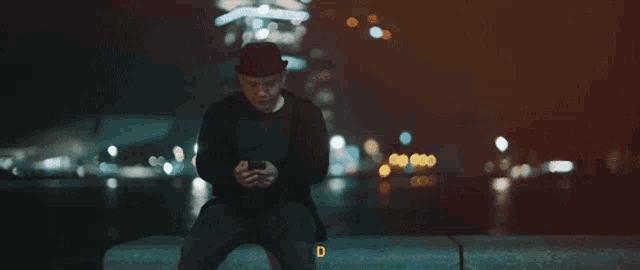 a man wearing a hat is sitting on a ledge with the letter b behind him