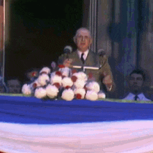 a man in a suit and tie is giving a speech in front of a crowd of people .