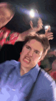 a man in a blue shirt is making a funny face while being photographed by another man .