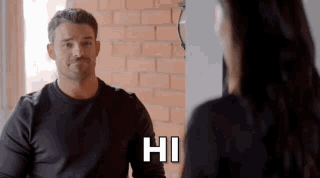 a man is sitting at a table talking to a woman and says hi .