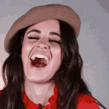 a woman wearing a hat and a red shirt is laughing .