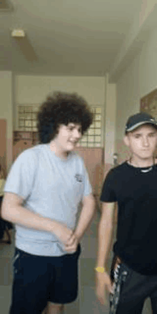 two young men are standing next to each other in a room and one of them has curly hair .