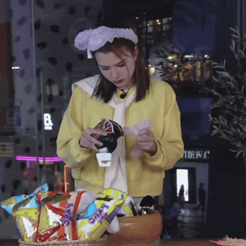a woman in a yellow sweater is standing in front of a basket of snacks including a bag of oreos