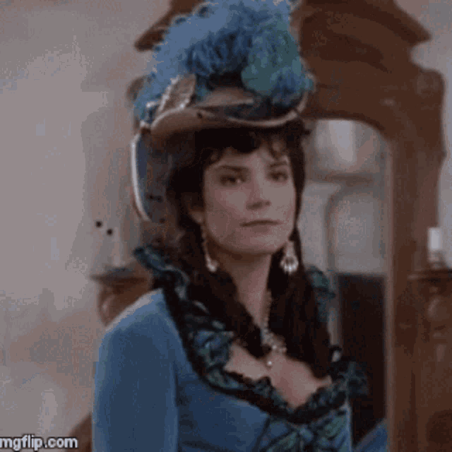 a woman wearing a blue dress and a hat with feathers is standing in front of a mirror ..