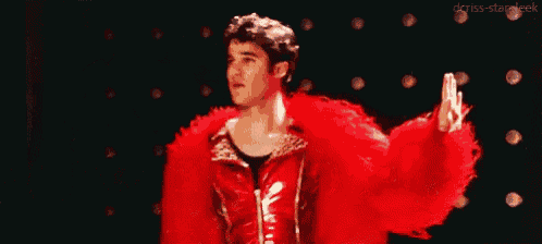 a man in a red fur coat is dancing on a stage in front of a row of lights .