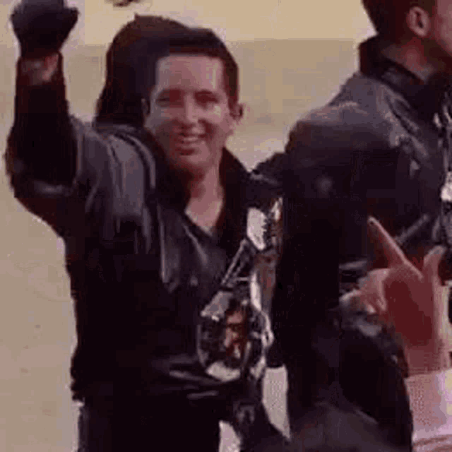 a man in a leather jacket is raising his fist in the air while standing next to another man .