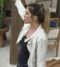 a woman in a white jacket is standing in a room with her arm up in the air .