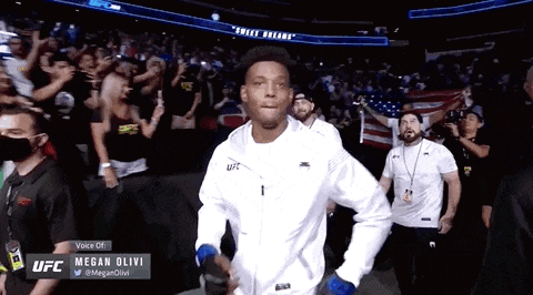 a man in a white ufc jacket walks into a stadium