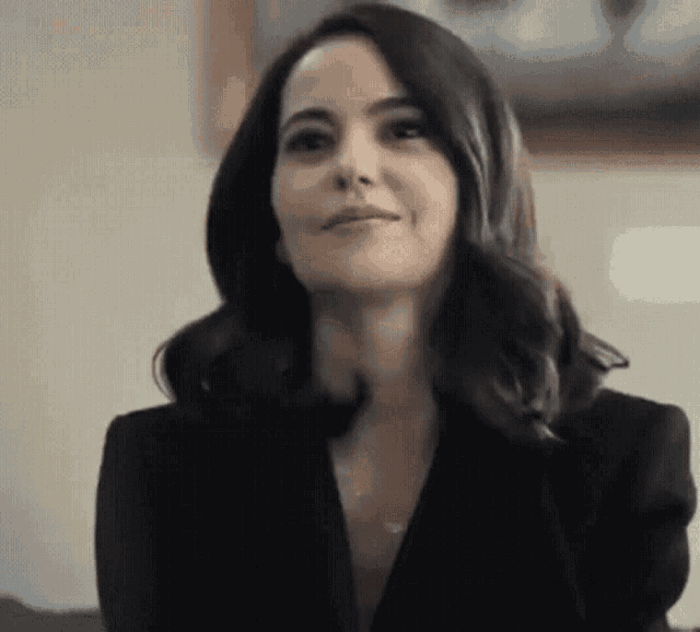 a woman in a black jacket is sitting on a couch and smiling at the camera .