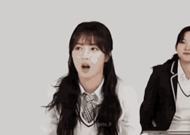 a girl in a school uniform is sitting next to another girl in a suit and tie .
