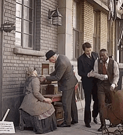 a man in a suit talks to a woman sitting at a table outside of a building