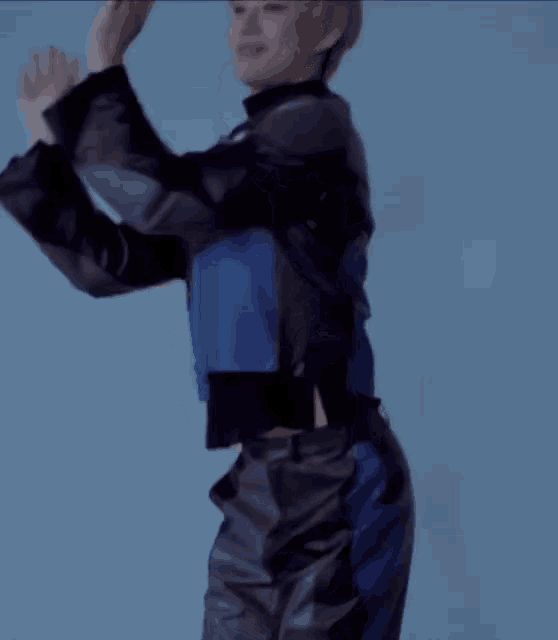 a woman in a blue jacket and black pants is dancing with her hands in the air