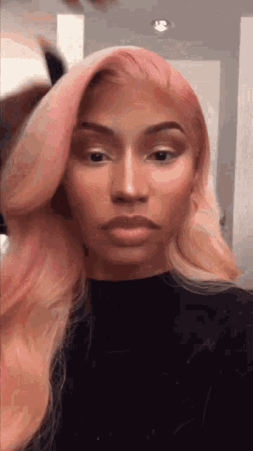 a woman with pink hair is wearing a black shirt and making a funny face .