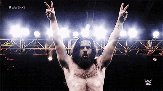 a man with a beard is giving a peace sign with his arms in the air in front of a wwe logo
