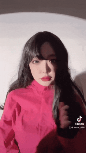 a woman in a red jacket is standing in front of a white wall and looking at the camera .