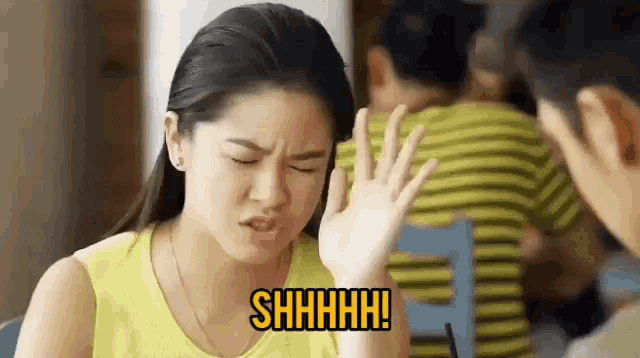 a woman in a yellow tank top is making a funny face while sitting at a table .